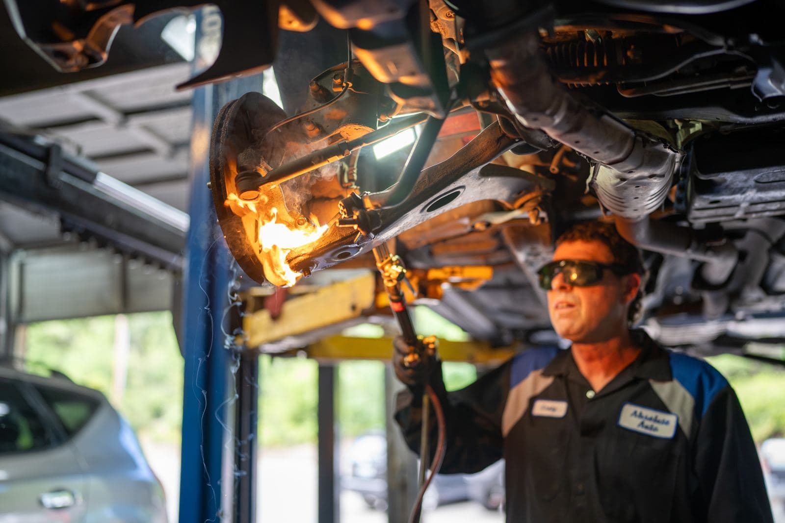 Technician using a torch on an exhaust component under a lifted vehicle