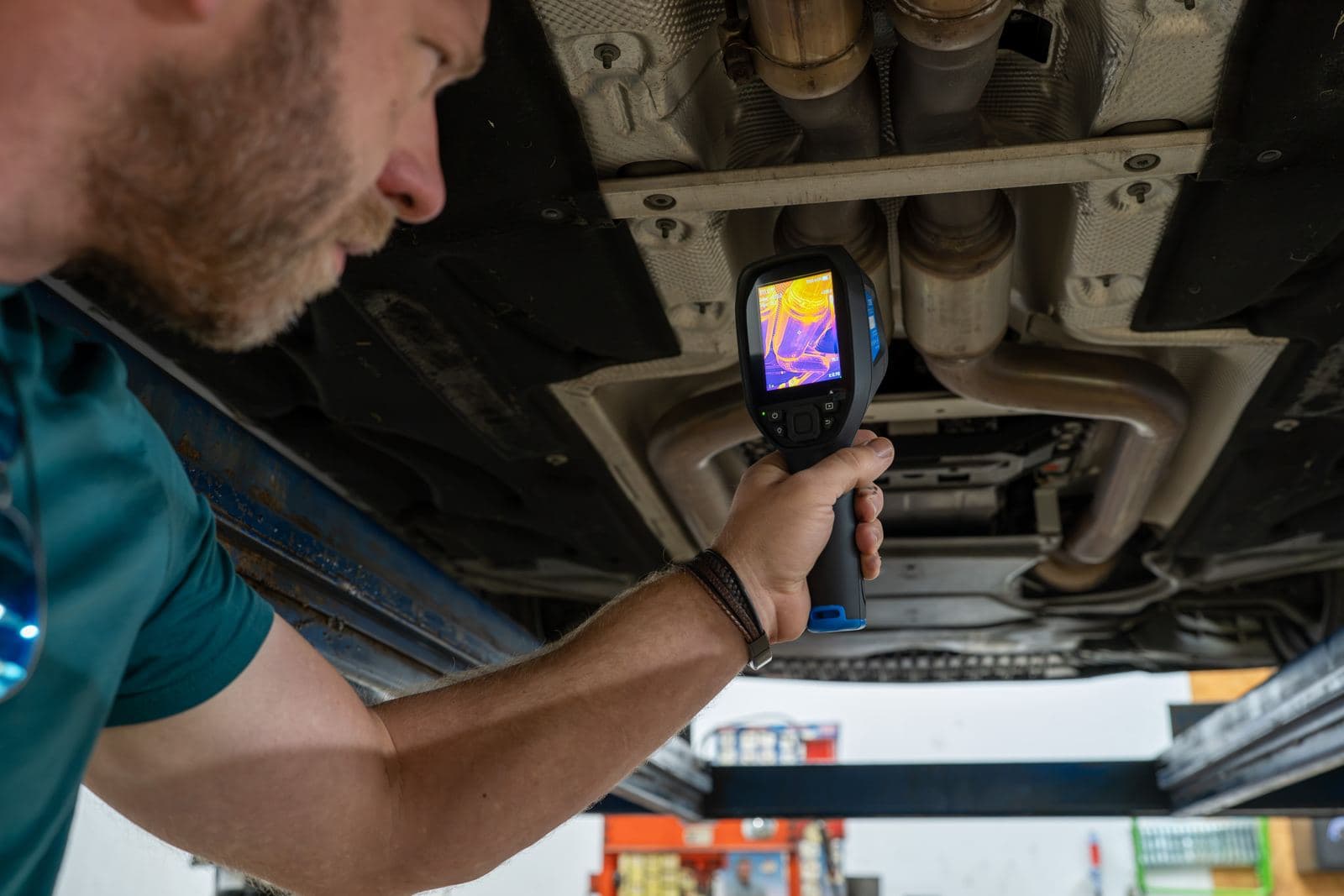 Technician scanning a vehicle's underside with a thermal imaging camera