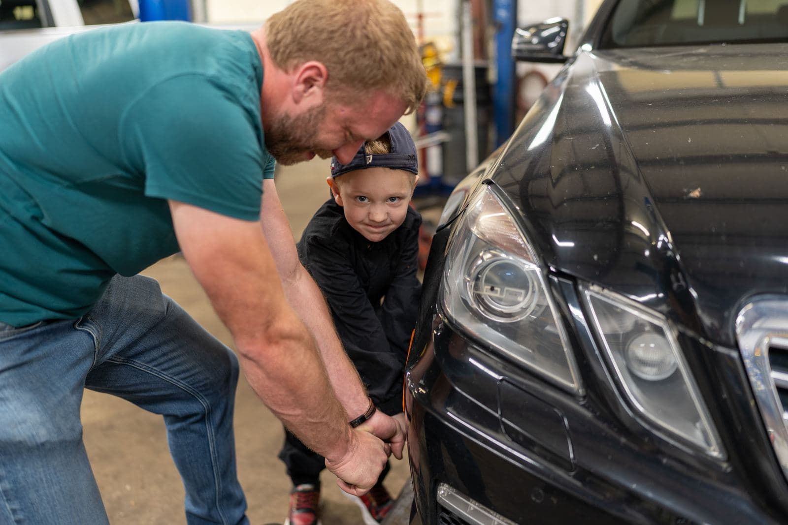 Shop owner teaching a junior crew member under the hood of a Mercedes