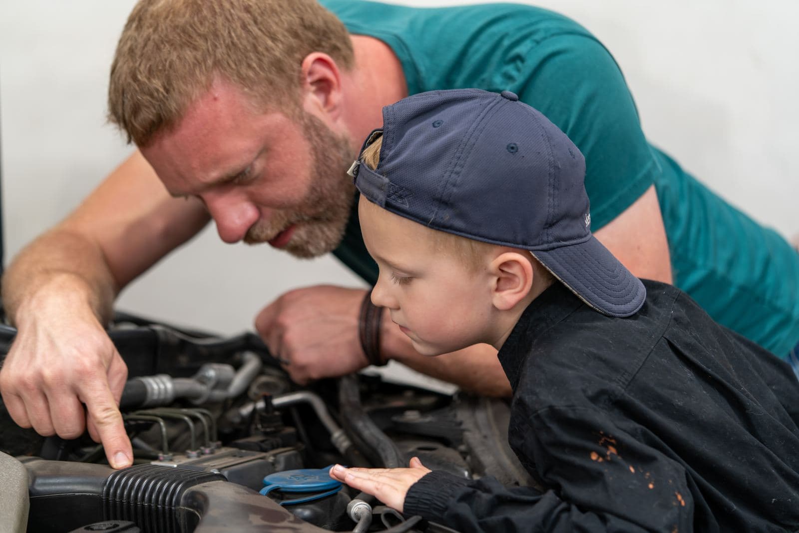 Shop owner teaching a junior crew member under the hood of a Mercedes