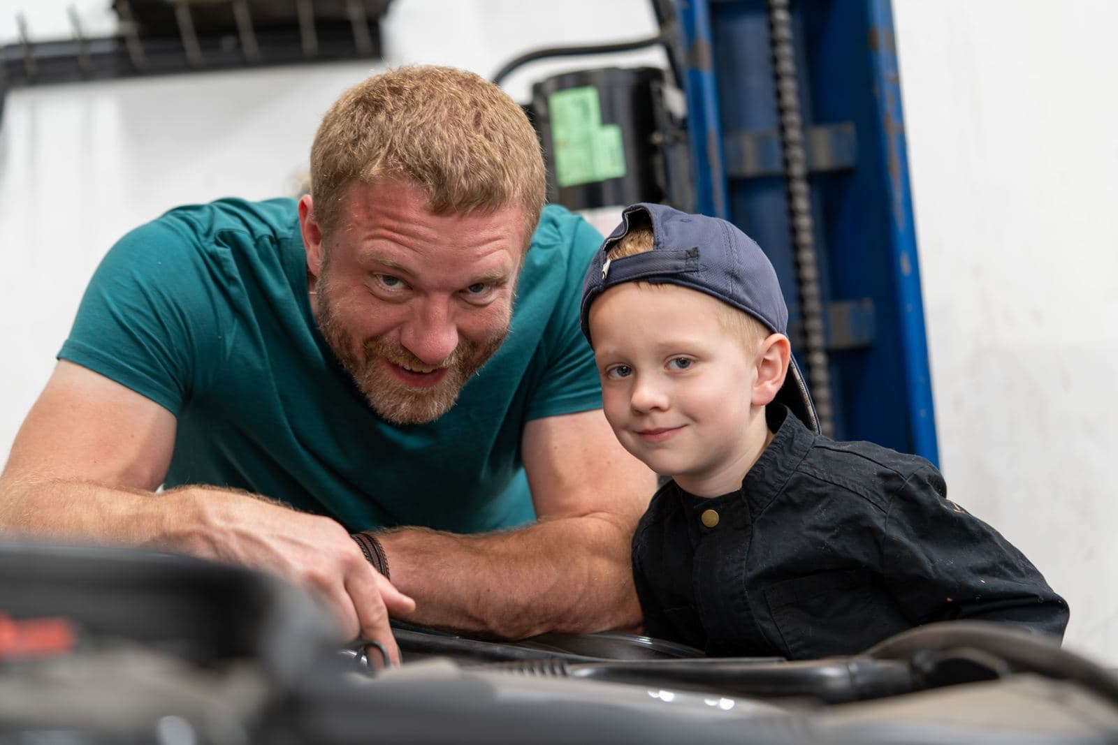 Shop owner teaching a junior crew member under the hood of a Mercedes